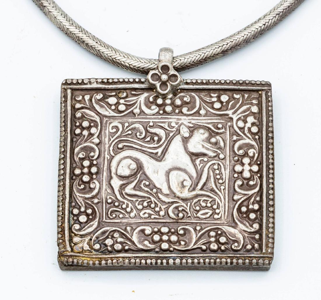 A Silver Amulet Pendant, Morocco, Late 19th Century: A Silver Amulet Pendant, Morocco, Late 19th Century Description: The pendant of square form, hammered and embossed with a depiction of an animal flanked by a floral border and suspended from a braided