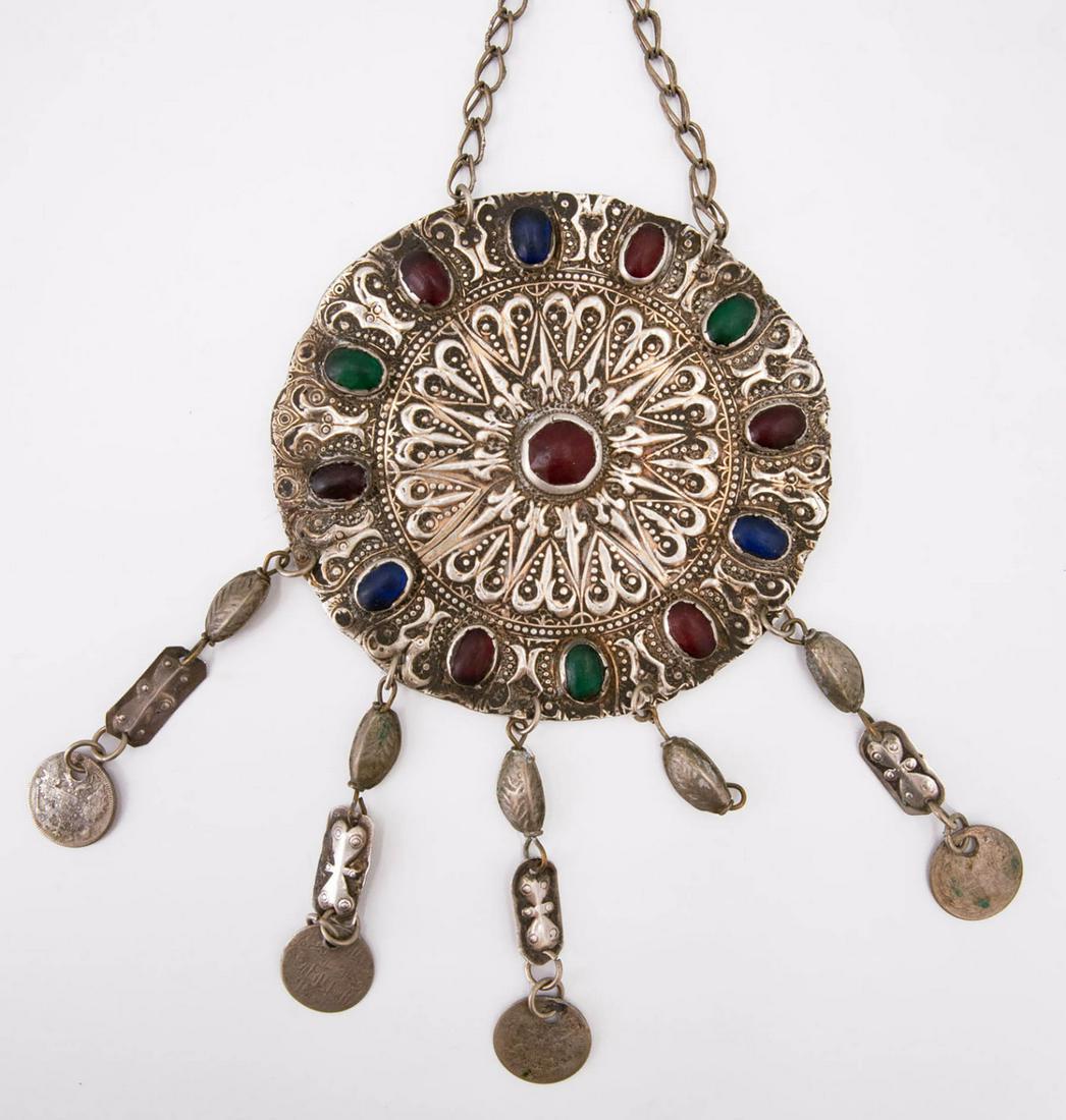 A Silver Breast Ornament, Uzbekistan, 19th Century: A Silver Breast Ornament, Uzbekistan, 19th Century Designed as a circular plate with hammered and embossed traditional motifs and set with colored stones.Terminating in a tassels with antique coins an