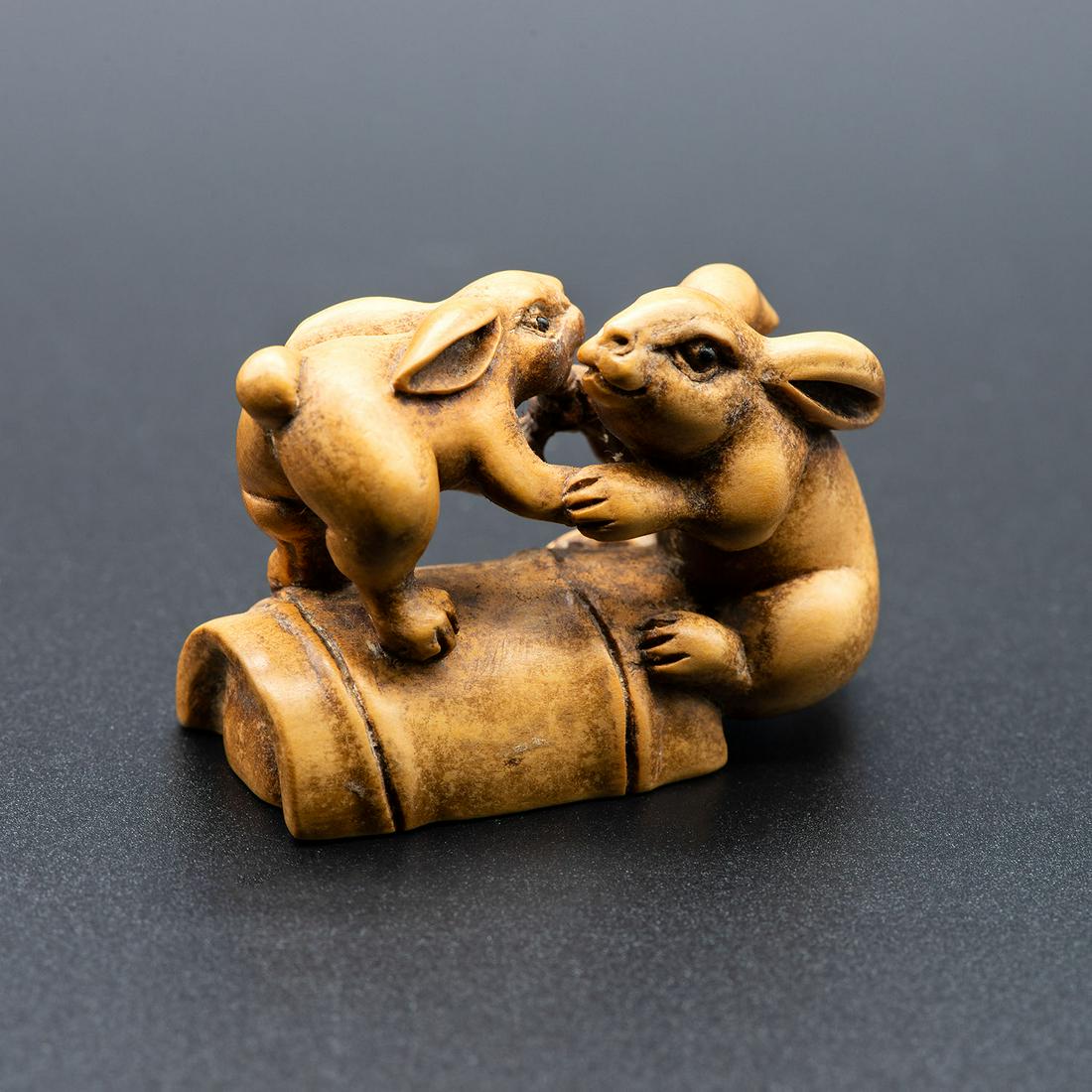 A Fine Carved Wood Netsuke of a Pair of Hares on a: A Fine Carved Wood Netsuke of a Pair of Hares on a Bamboo, Japan, 19th century Signed SOKKOU (on the underside). Height: 4.5 cm Condition: For a detailed condition report, please contact us at info@ha