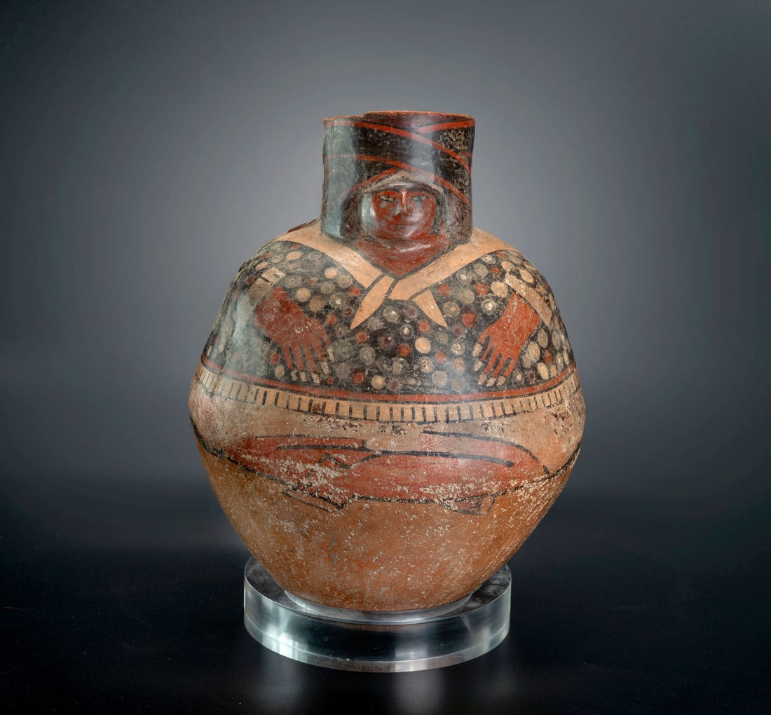 A Spouted Bottle Depicting a Seated Male Figure, Late Nasca, Peru, 300-600 CE: A Spouted Bottle Depicting a Seated Male Figure, Late Nasca, Peru, 300-600 CE Spouted effigy bottle representing a man with legs crossed and hands resting on his abdomen. Only his face is rendered in