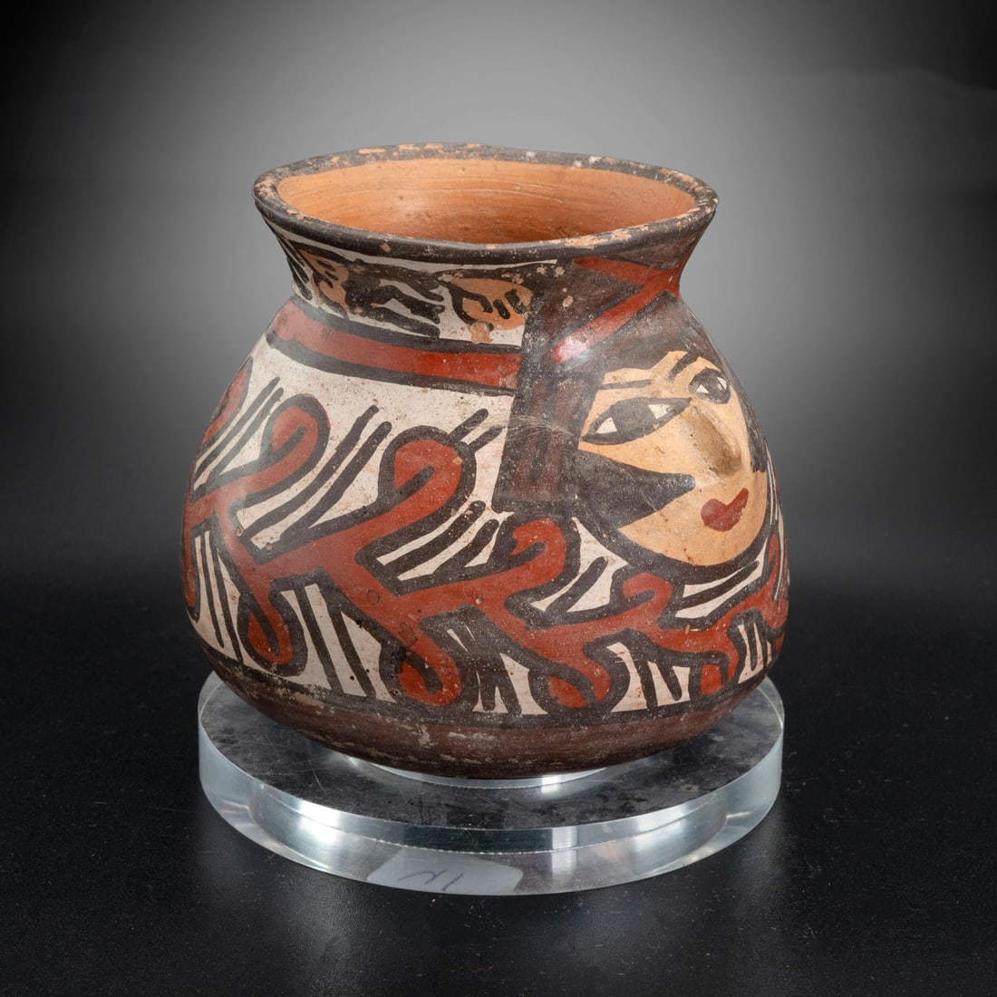 A Spouted Jar Decorated with a Depiction of a Human Face, Late Nasca, Peru, 300-600 CE: A Spouted Jar Decorated with a Depiction of a Human Face, Late Nasca, Peru, 300-600 CE Height: 10 cm For more details on this lot refer to the following number in the link: num 160, p. 157 (