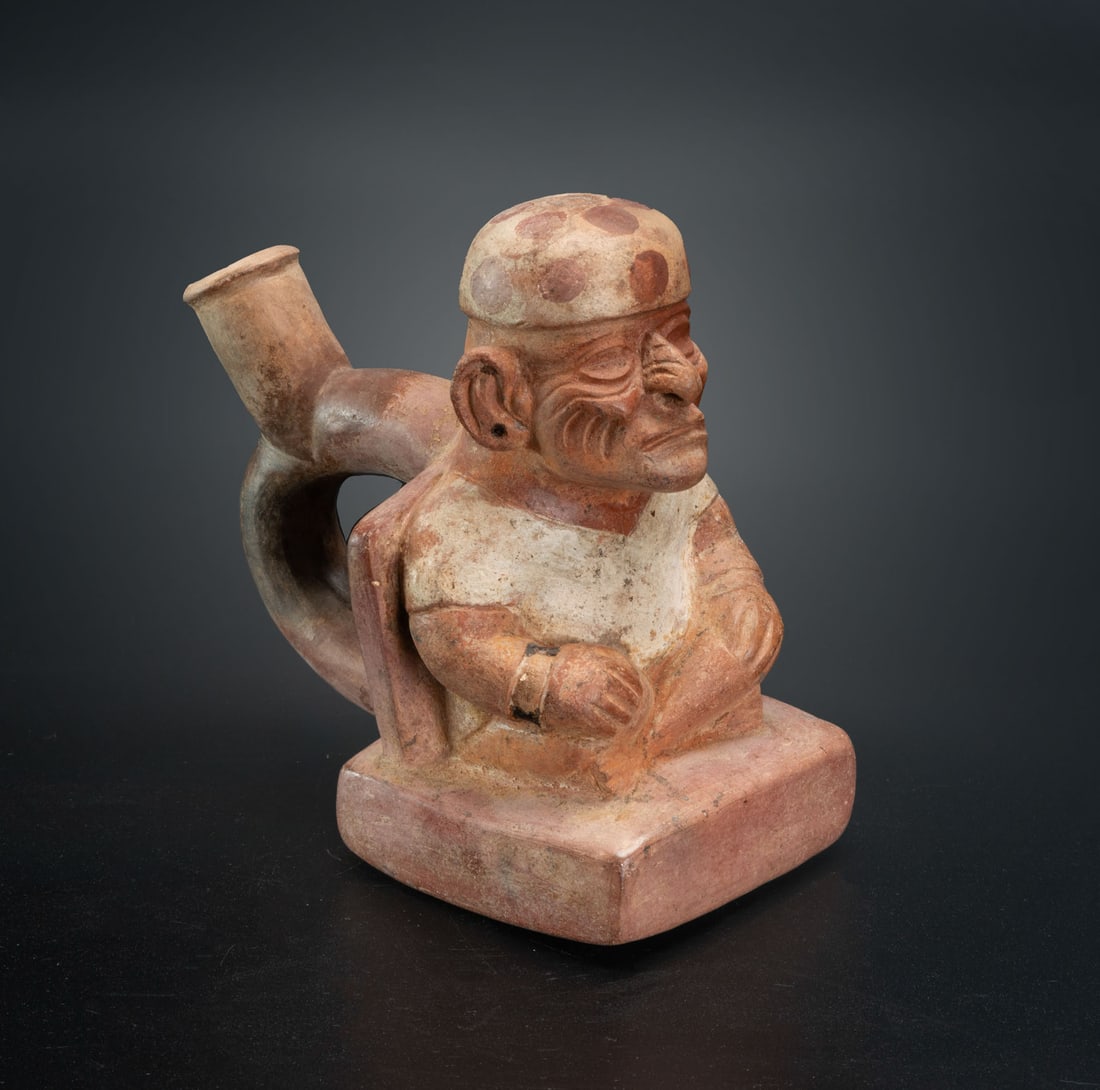 A Spout Effigy Bottle: Seated Priest with a Headdress, Moche, Peru, 600-900 CE: A Spout Effigy Bottle: Seated Priest with a Headdress, Moche, Peru, 600-900 CE Height: 13.8 cm Provenance: Jean Pierre Cottier and Fiorella Cottier-Angeli, Geneva, Switzerland. Purchased by Yossef Mai