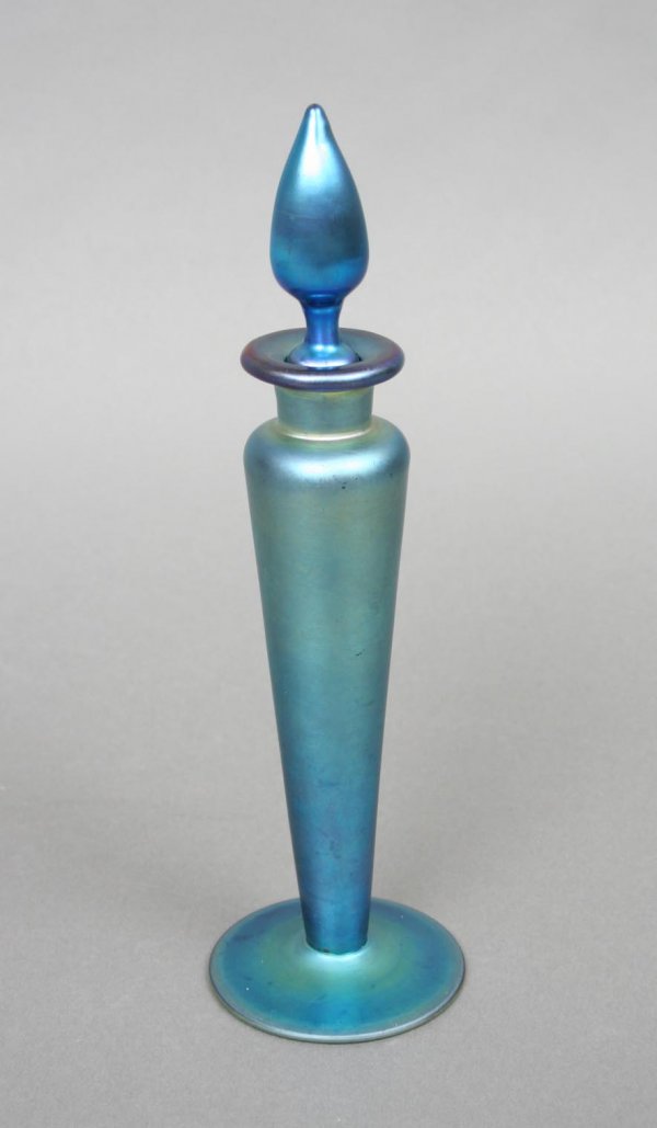 Steuben Blue Aurene Perfume Bottle: Steuben, blown in iridescent blue glass, of baluster form with an ogee form stopper, signed Aurene 1414. 7 3/4"H. Condition: tiny flake to collar, otherwise excellent.