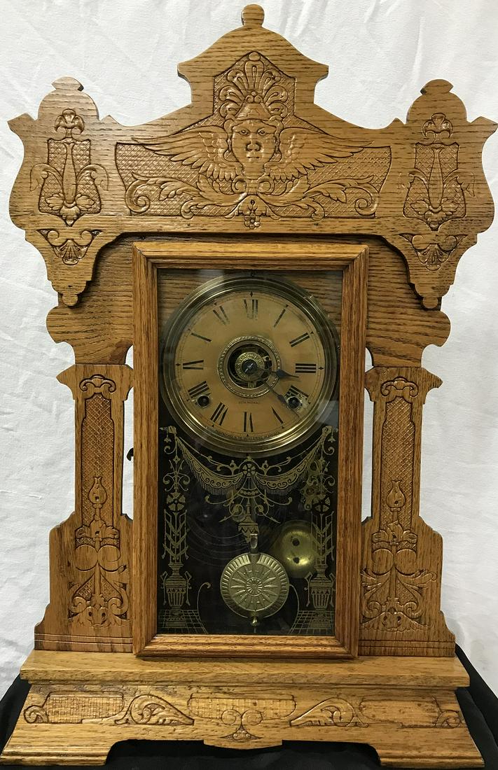 Clock - Seth Thomas Kitchen Clock: Oak Frame Kitchen Clock. Original paper face on brass backing. Ornate carving to wood cabinet w/ladies face and crown at top of cabinet with wings on side of face. Has pendulum and Key. Not running. G