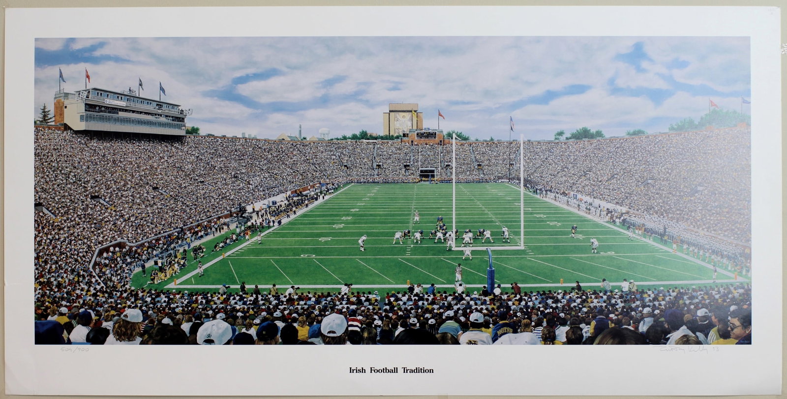 Lithograph "Irish Football Tradition" by Tim Kelly: Large artist-signed limited edition lithograph titled Irish Football Tradition by Tim Kelly, dated 1993 and numbered 504/900. This panoramic depiction of a packed Notre Dame football stadium captures 