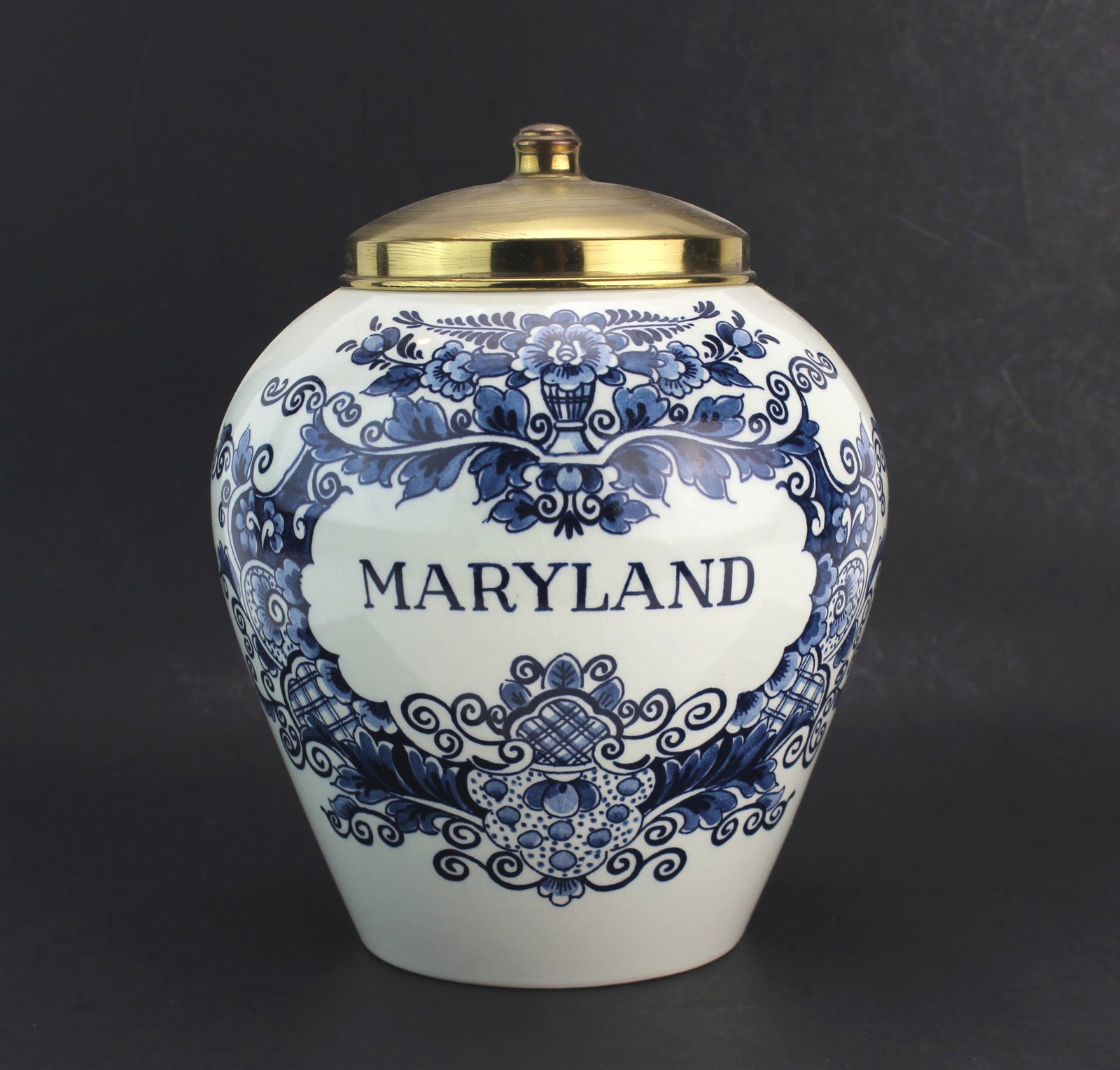 Royal Goedewaagen Blue Delft Maryland Jar: A hand-painted porcelain jar from Royal Goedewaagen, crafted in Holland in traditional Delft Blue style. The jar features floral scroll motifs and the word "Maryland" on the front, with a brass lid an