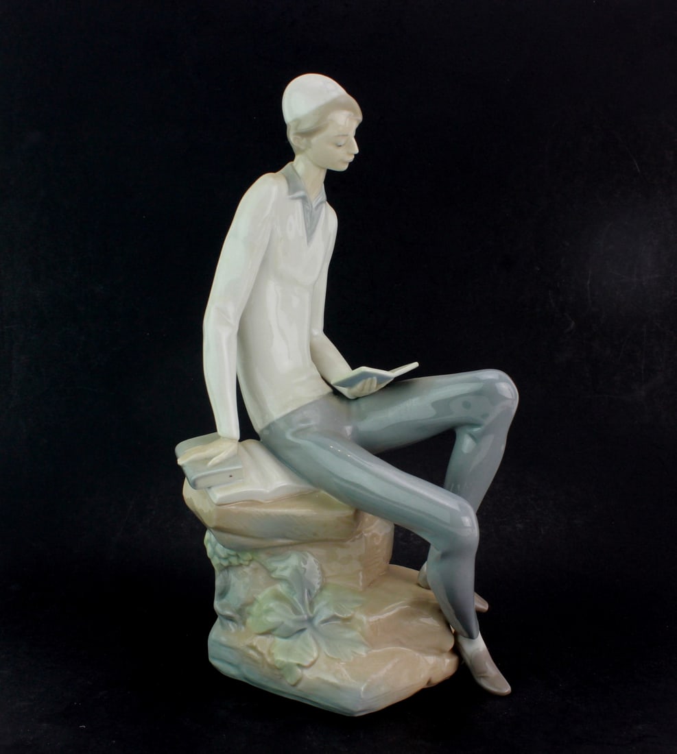 Lladro Hebrew Student Jewish Boy Figurine: Lladro porcelain figurine of a young man seated with a book, finished in soft pastel tones and glossy glaze. Handmade in Spain and marked with the Lladro logo. Dimensions: 11 1/5 X 6 X 5 inches.