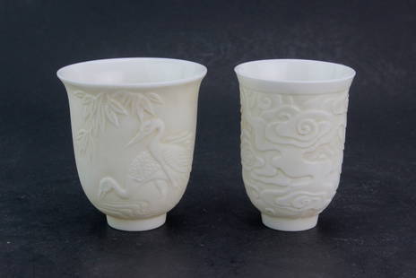 Two Chinese White Porcelain Tea Cups: A pair of blanc de chine porcelain tea cups, one decorated with cranes and bamboo, the other with cloud motifs. Finely carved in low relief, with smooth glazed interiors. Likely late Qing or Republic