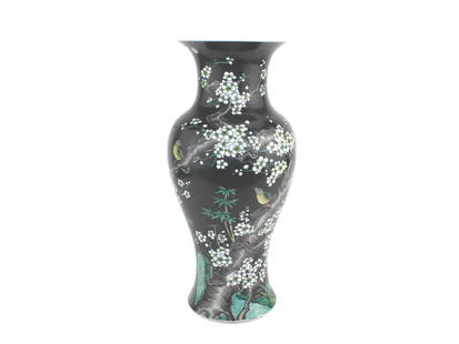 CHINESE BLACK GLAZED FAMILLE NOIRE VASE: A Chinese porcelain vase with a black glaze, decorated with white plum blossoms, green bamboo, and birds perched on gnarled tree branches. The intricate enamel painting reflects famille noire style. T