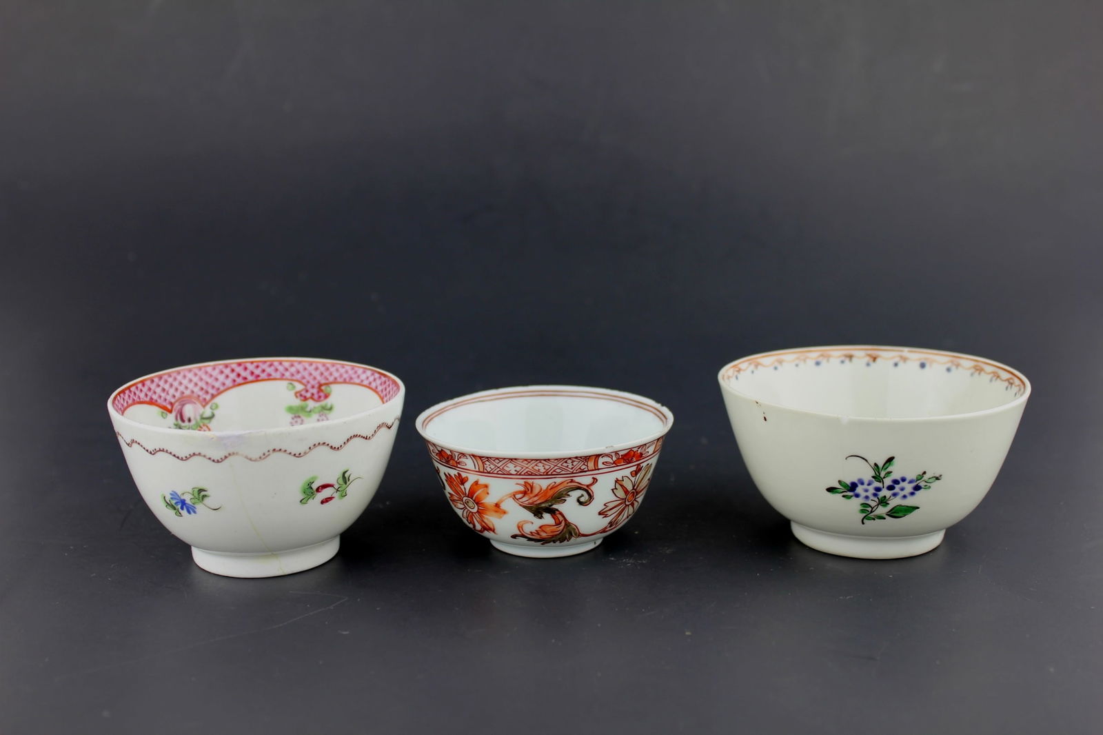 GROUP OF THREE CHINESE EXPORT TEA CUPS: Three 19th century Chinese export teacups, each hand-painted with floral designs in famille rose and iron-red palettes. One bowl has a hairline crack, others features a rim chip, and all show age-rela