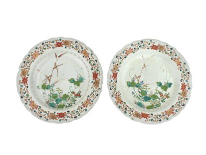 TWO CHINESE FAMILLE ROSE PLATES: A pair of Chinese Qing Dynasty famille rose porcelain plates, each featuring central floral and bamboo motifs with a colorful enamel border of scrolling flowers. The plates have scalloped rims and sho