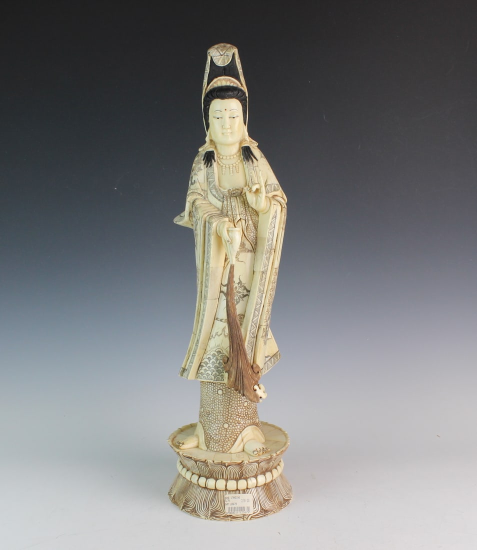 Large Carved Bone Statue of Guanyin: Carved bone statue of Guanyin on lotus pedestal with fine etched details, painted accents, and fitted brocade case. Shows minor wear and natural age lines. Size: 20 in. (H) X 6 in. (L) X 5 1/2 in. (W)