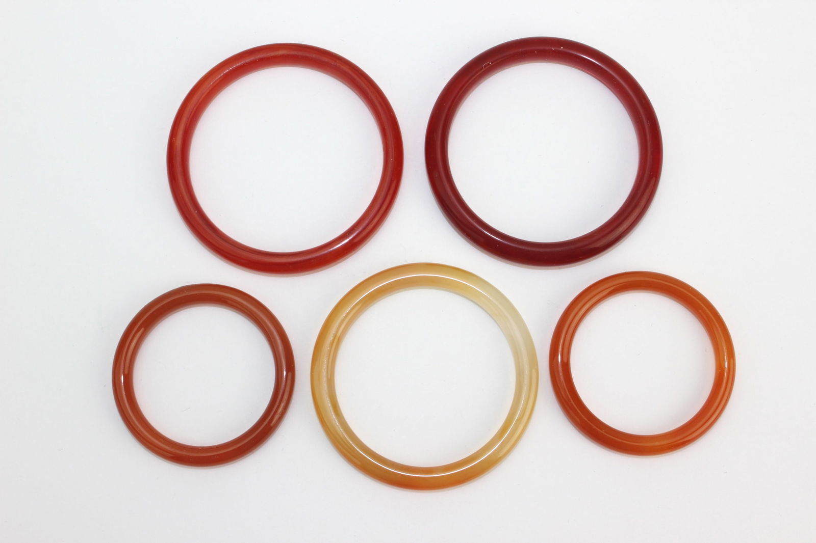 Five Mixed Color Hardstone Bangles: A group of five hardstone bangles in red, orange, and honey yellow tones, smoothly polished with natural color variations. Minor surface wear, overall in good condition. Largest approx. 67.8 mm (outer