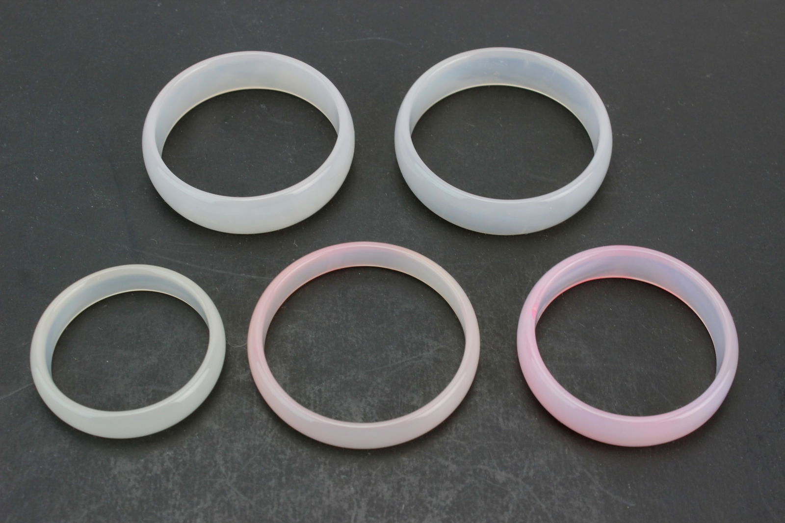 Group of Five Translucent Hardstone Bangles: A collection of five hardstone bangles in white and pale pink tones, smoothly polished with natural translucency and soft color variations. Minor inclusions and light wear, overall in good condition.