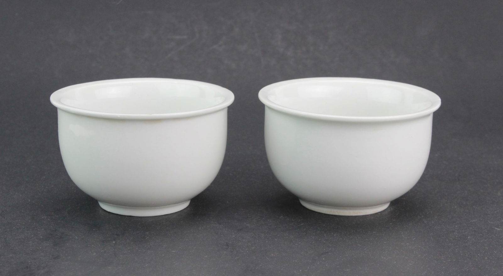 Two Chinese Blanc de Chine Porcelain Tea Cups: A pair of plain white glazed porcelain teacups with flared rims and smooth bodies. One has a small rim chip. Each cup measures approximately 3 1/4 in. (D) X 2 in. (H).