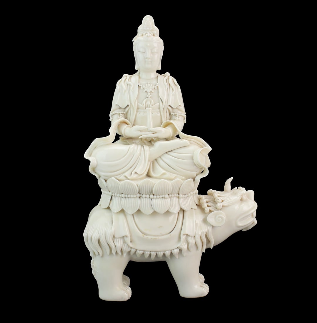 Blanc de Chine Guanyin on Mythical Beast: Chinese Blanc de Chine figure of Guanyin seated in meditation atop a lotus throne raised on a mythical beast. The serene deity is shown holding a vase, adorned with flowing robes, beaded jewelry, and
