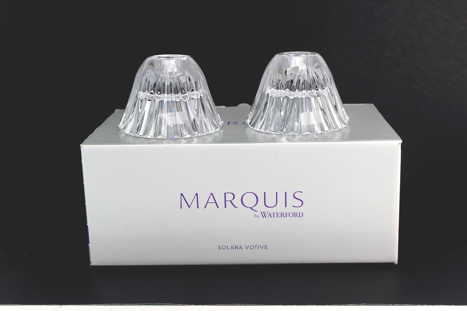 Marquis by Waterford Solara Votive Pair: A pair of Marquis by Waterford Solara crystal votive holders made of clear lead crystal with faceted detailing. Each votive measures approx. 4 in. (D) x 2 in. (H) and comes with the original