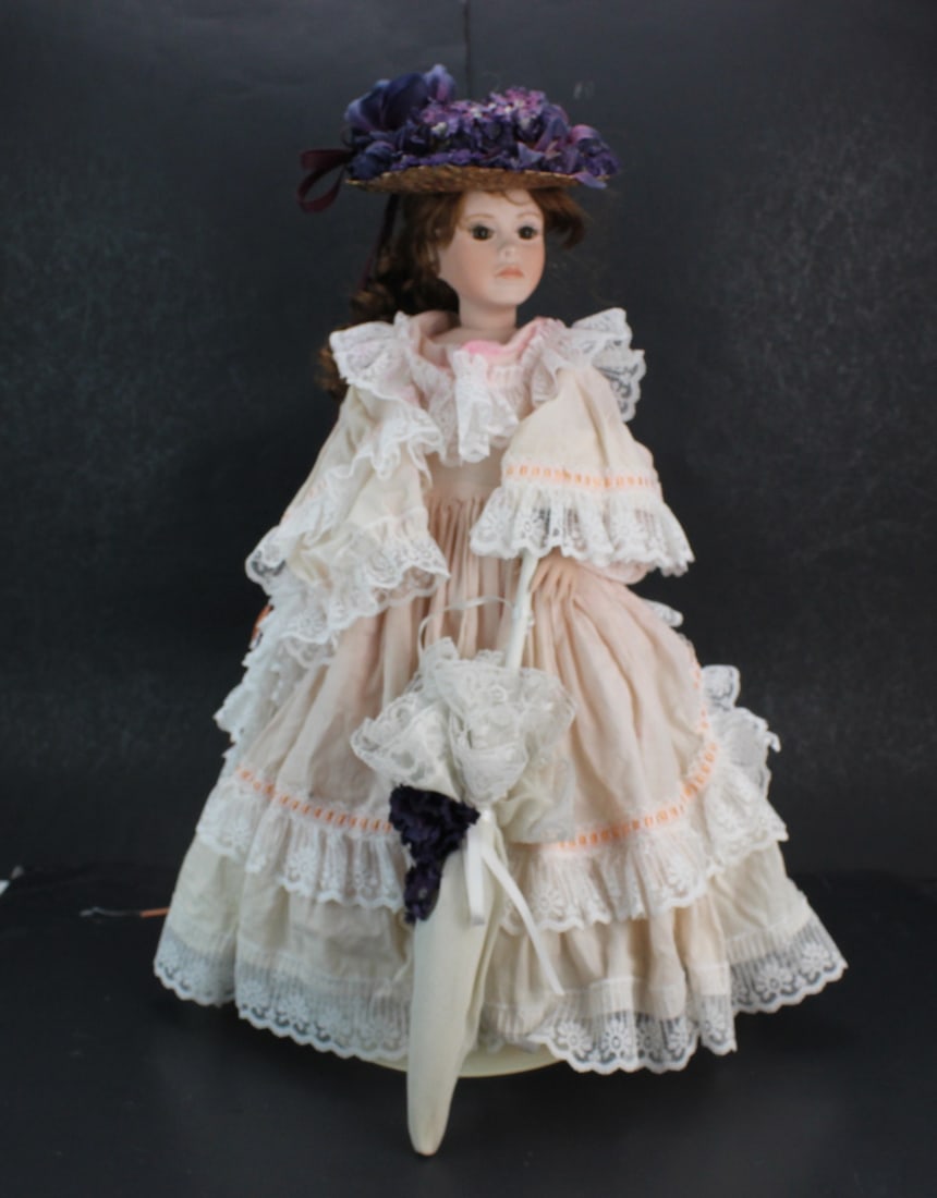 Signed Porcelain Doll in Victorian Dress: Signed porcelain doll dressed in a layered Victorian-style gown with lace trim, straw hat with floral decoration, and parasol. Numbered 4 of 100 Limited edition. Size: 21 in. tall. Condition: light