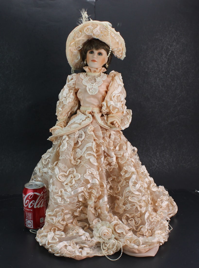 Signed Porcelain Doll in Victorian Peach Dress: Signed porcelain doll with painted facial features, brown styled hair, and elaborate Victorian-style peach lace dress with matching hat and accessories. Size: 21 in. tall. Condition: light surface