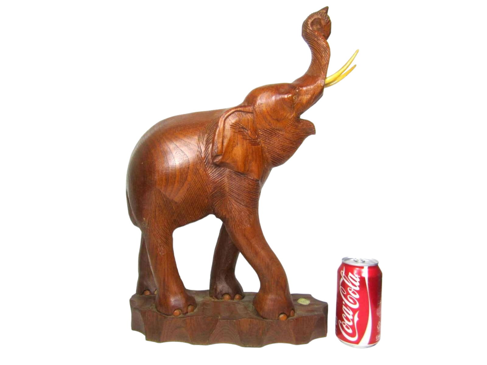Hand-Carved Teak Wood Elephant Statue: A hand-carved teak wood elephant statue from Thailand. It depicts a standing elephant with its trunk raised and bone-colored tusks, on a textured base, measuring 20 in. (H) x 13 in. (L) x 7 in. (W).