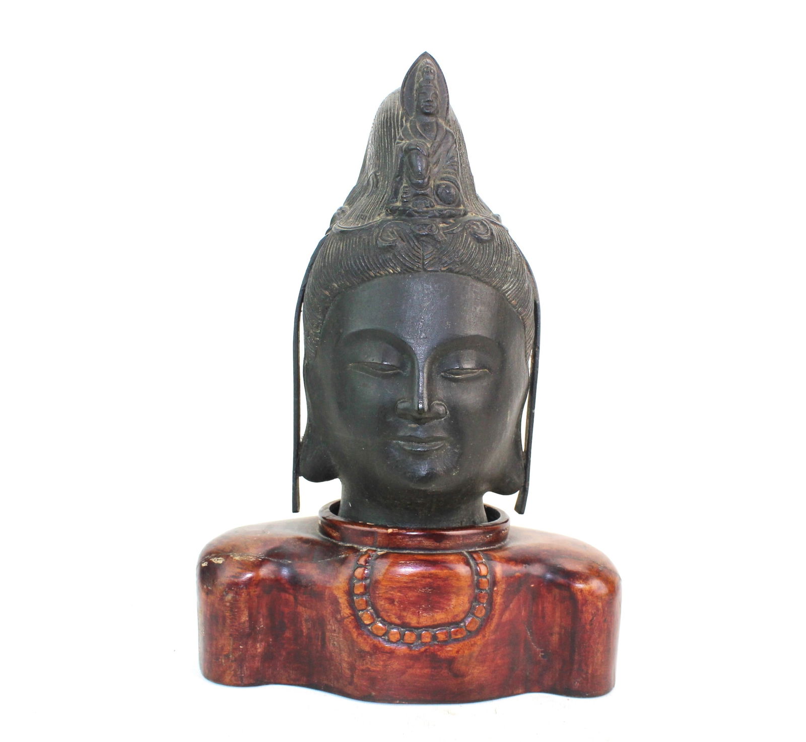 Bronze Buddha Head on Carved Wood Stand: Bronze Buddha head with calm expression on a carved wooden stand, showing natural patina, minor wear, and verdigris; wood base has age-related wear and cracks but is stable. Size: Buddha: 9 1/2 in. (H