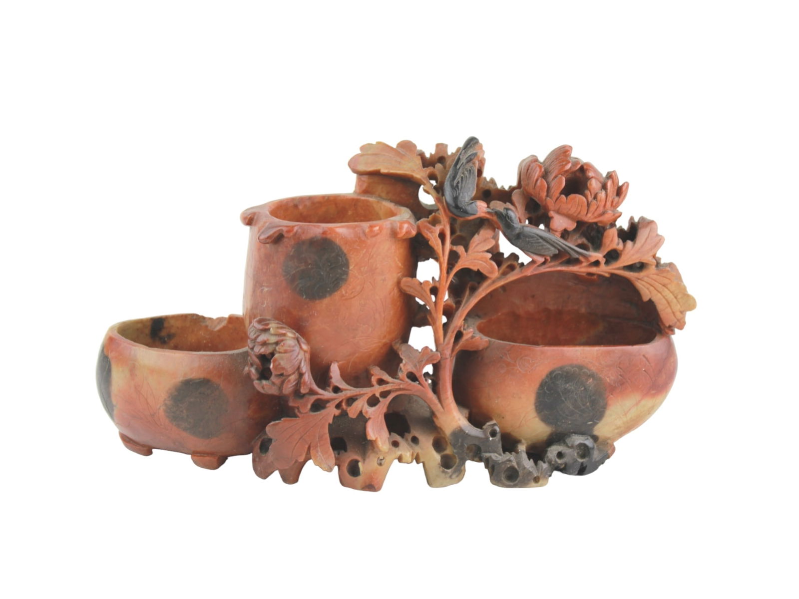 CHINESE CARVED SOAPSTONE SCHOLAR DESK VASE: A reddish-orange soapstone vase with black inclusions, intricately carved with flowers, leaves, and birds. It consists of three interconnected vessels, featuring detailed natural rock formations.