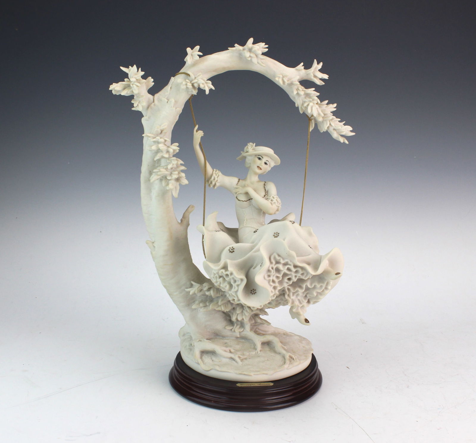 Armani Young Lady on Swing Figurine: Charming Giuseppe Armani porcelain figurine titled “Young Lady on Swing,” dated 1993 and set on a polished wood base. Measures approx. 13 in. (H) X 6 in. (W) X 10 in. (L). Excellent overall