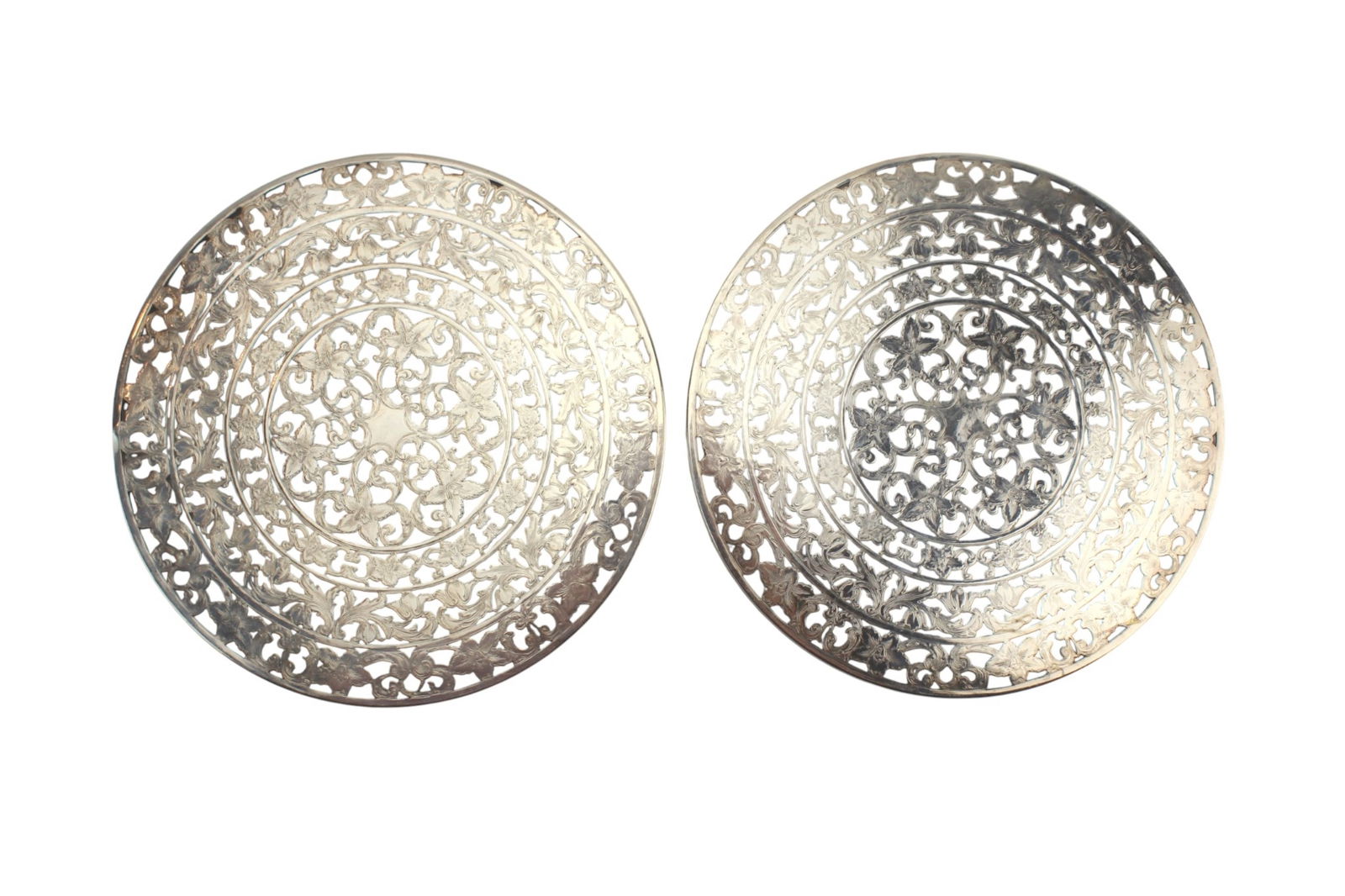Pair of Webster Sterling Silver Trivets: Set of two round sterling silver trivets by Webster, featuring intricate pierced floral and scrollwork decoration. One with glass bottom. Each measures approximately 10 in. (D), with a combined