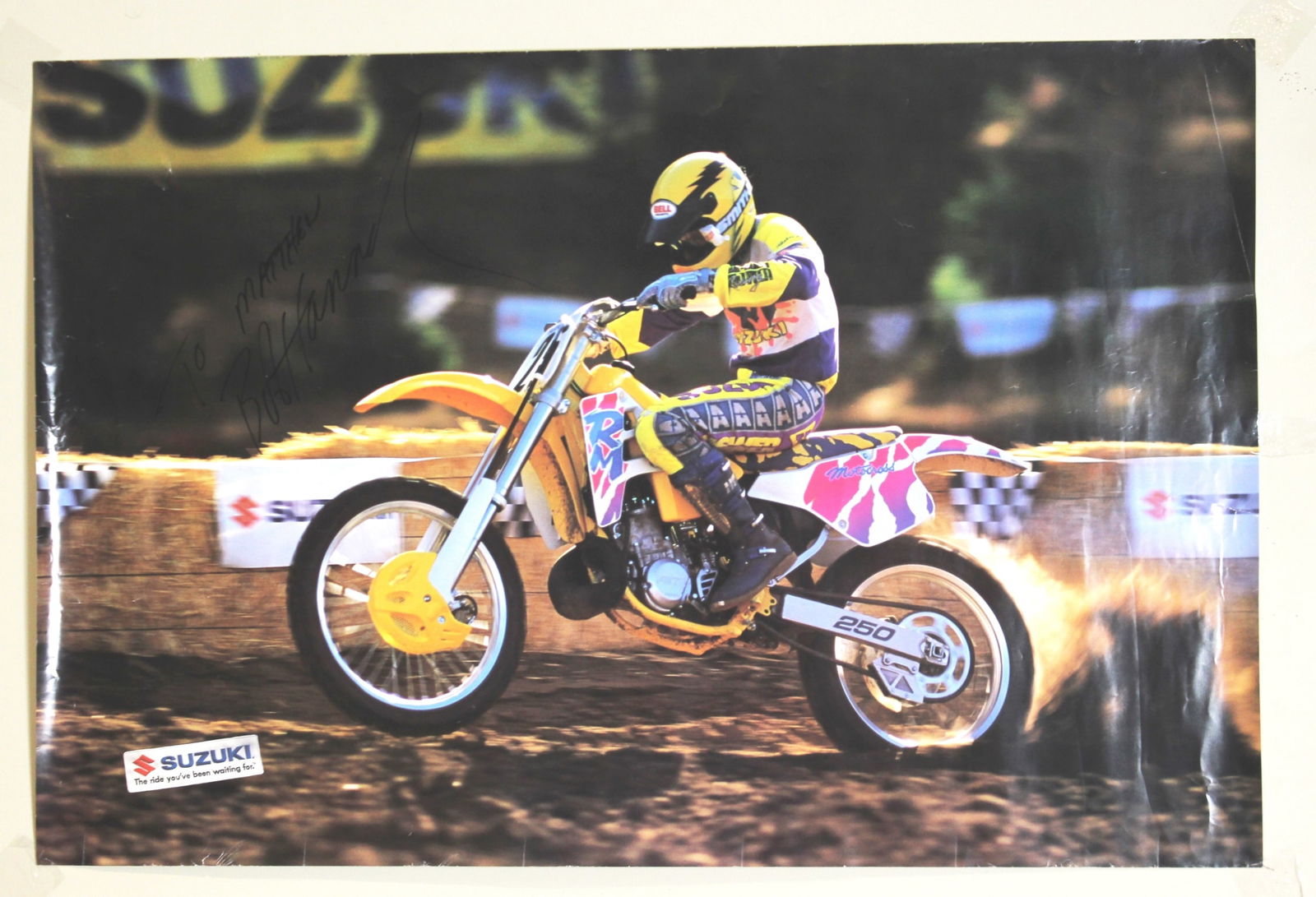 Bob Hannah Signed Suzuki Motocross Poster: Original Suzuki motocross action poster featuring a rider in full race gear, signed in black marker by Bob Hannah. Measures 24 X 36 in. Condition is good overall, with visible handling wear including
