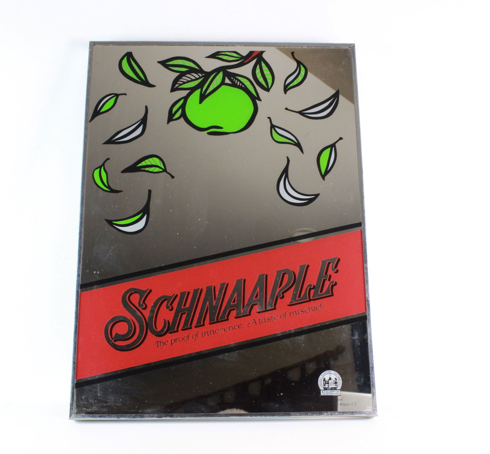 Germany Schnaple Liqueur Advertising Wall Mirror: Vintage mirror sign for Schnaaple apple liqueur, featuring vibrant graphics and the slogan “The proof of innocence. A taste of mischief.” Made in the USA for an imported German product.