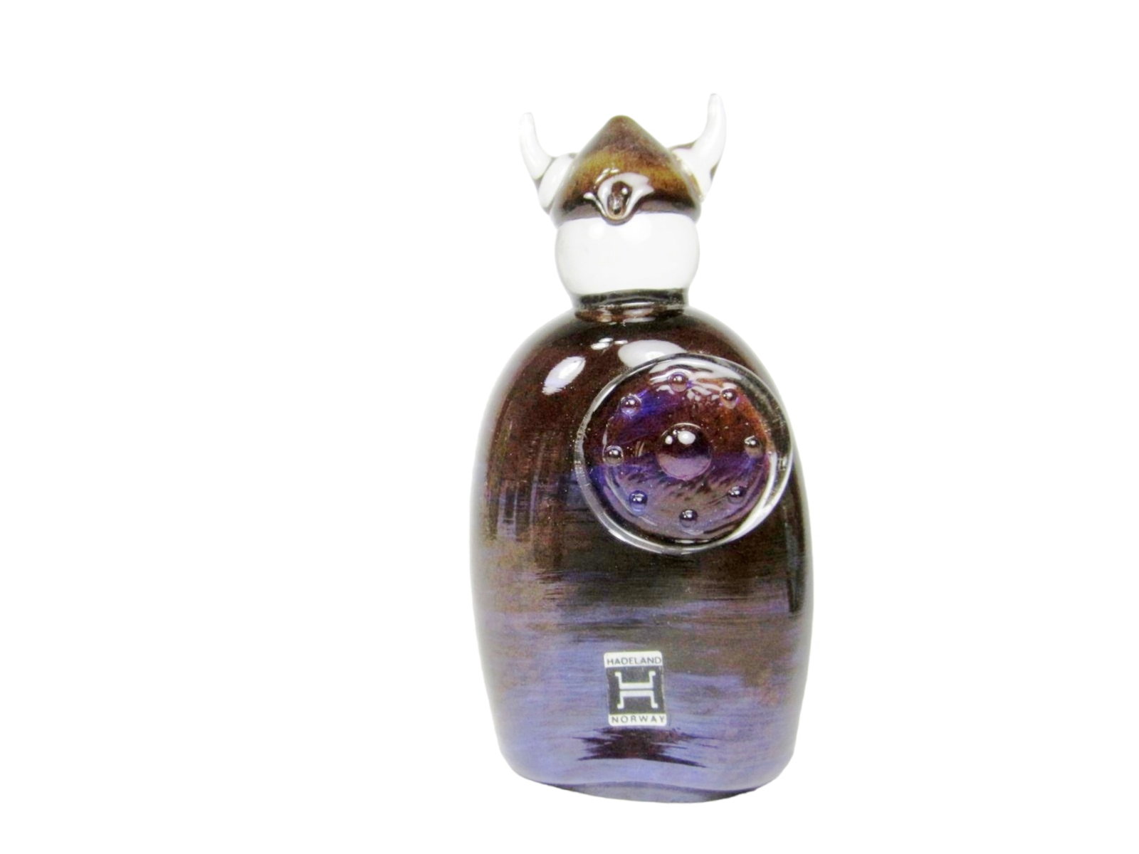 Hadeland Norway Glass Viking Figure Perfume Bottle: Handcrafted by Hadeland Glassverk in Norway, this figural glass bottle depicts a Viking with horned helmet and shield. It features a deep iridescent purple hue, original label, and engraved flag emble