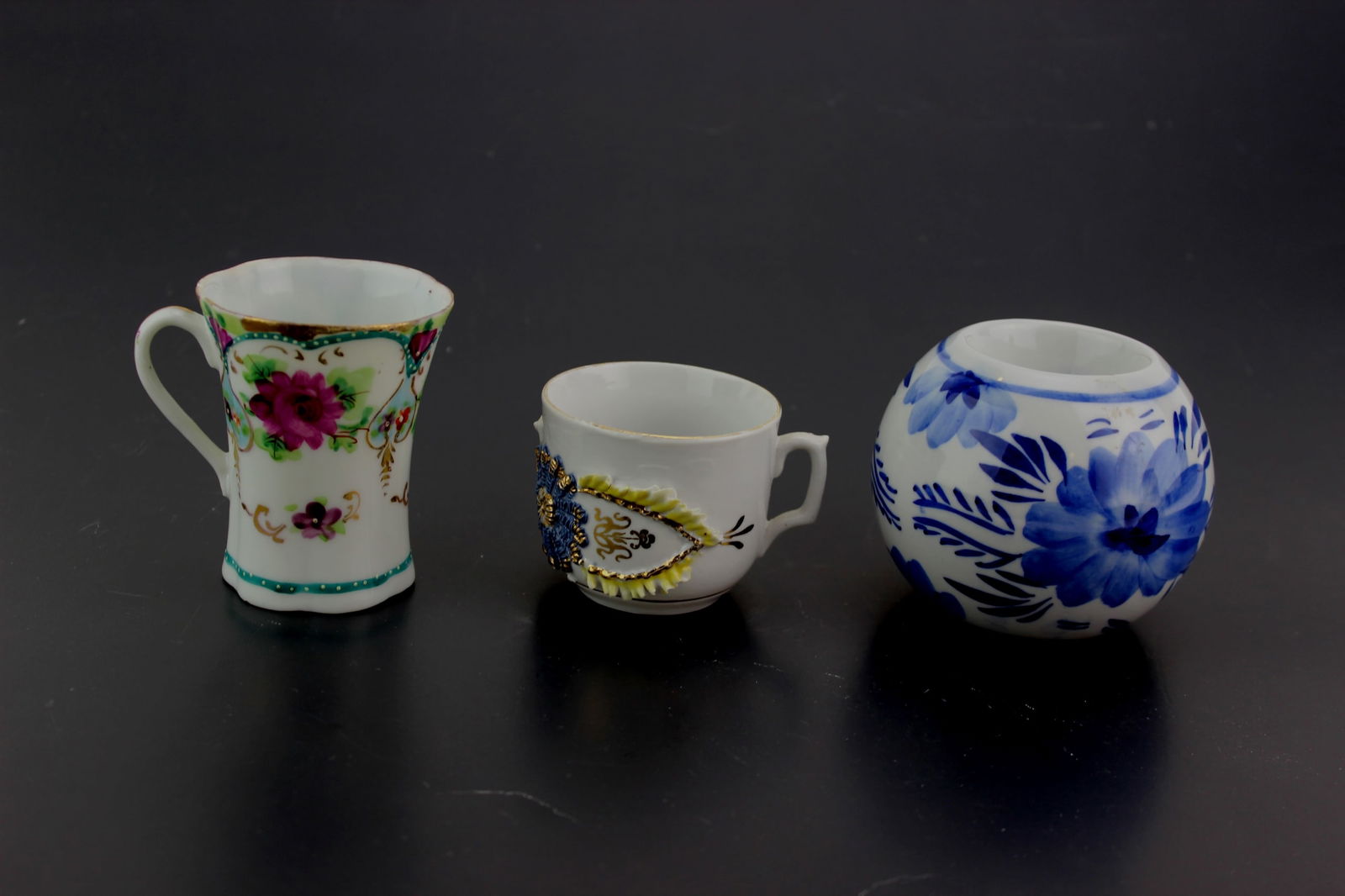 Three Porcelain Table Items: Set of three decorative porcelain pieces: a floral demitasse mug with gilt accents in 3 inches tall, a rococo-style encrusted cup with raised decoration 2 in. tall, and a blue-and-white round jar with