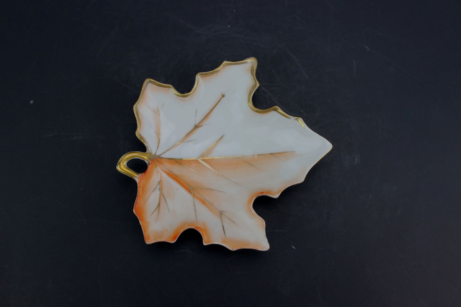UCAGCO Leaf-Shaped Porcelain Dish: Leaf-shaped porcelain dish with gold trim and autumn colors, made by UCAGCO in Occupied Japan (circa 1945–1952). Dimensions: 4 1/2 in. (L) X 4 in. (W). Provenance: Originally purchased from the