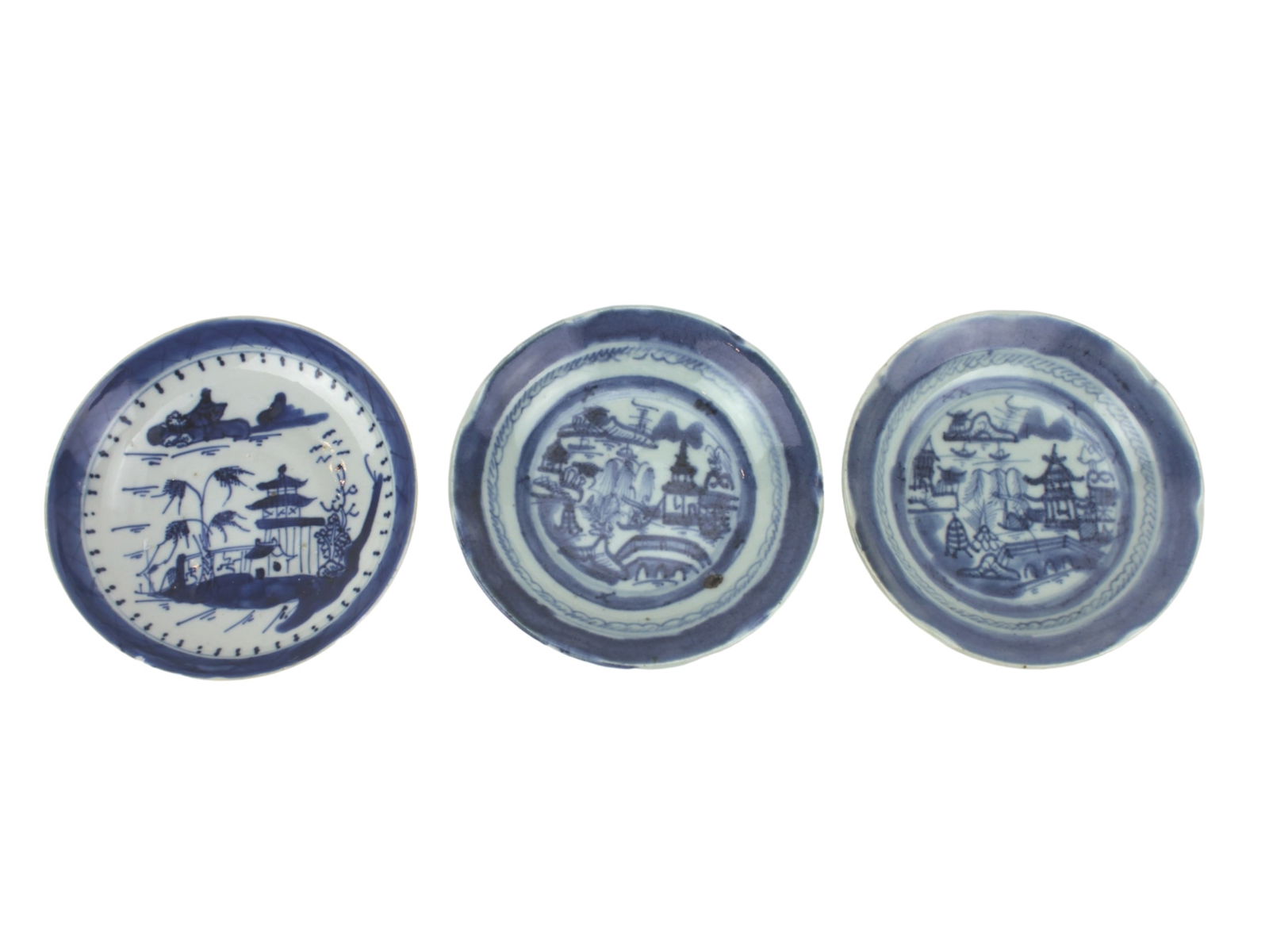 Three Canton Blue And White Saucers: Set of three late Qing porcelain saucers painted in underglaze blue with landscapes of pavilions, trees, and rivers. Unglazed foot rims with kiln grit. One saucer with small rim chip; others in good c