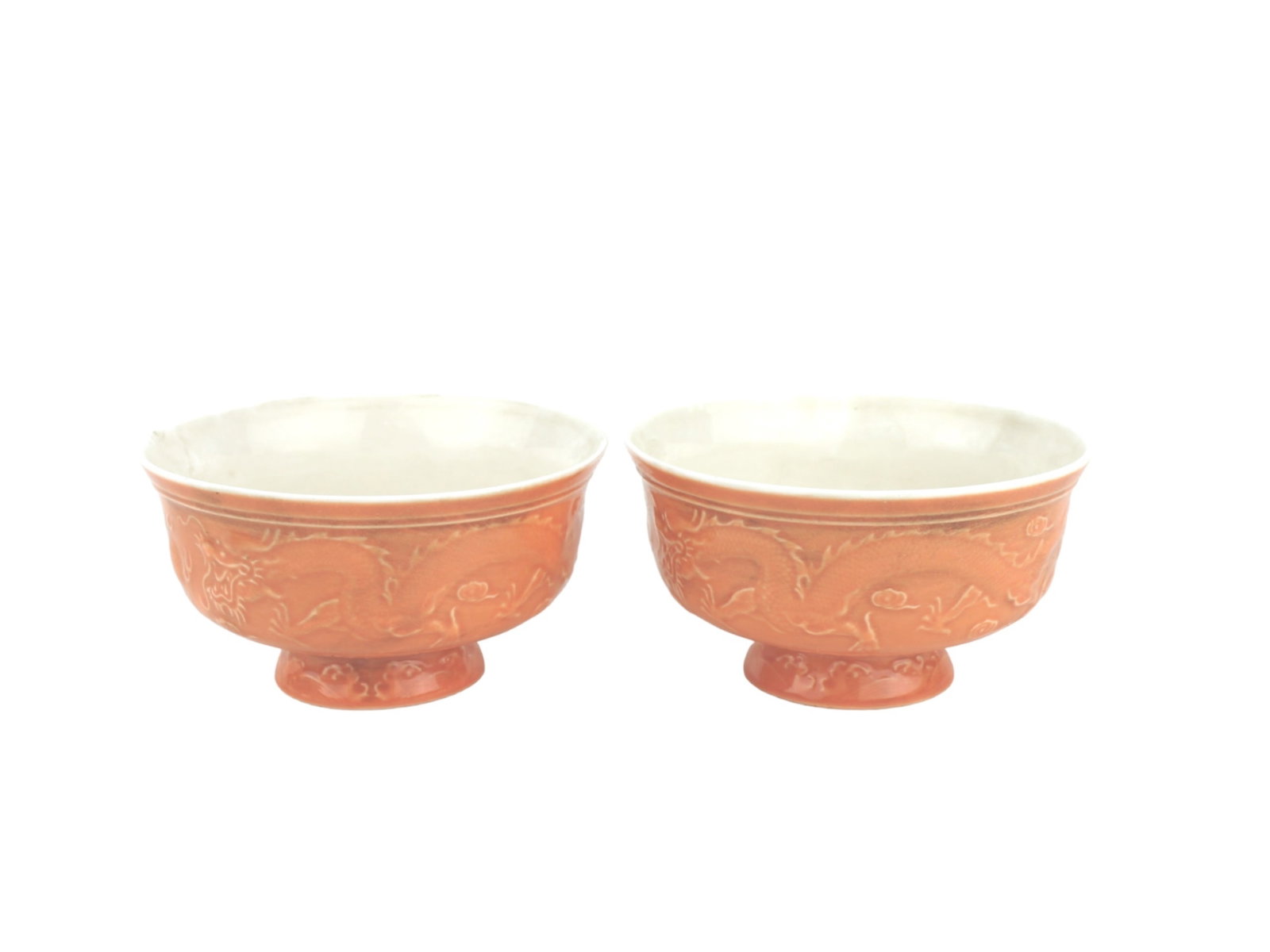 Pair of Red-Ground Chinese Porcelain Dragon Bowls: A matched pair of Chinese porcelain bowls with white glazed interiors and red-ground exteriors, each decorated in relief with dragons chasing flaming pearls. Set on raised footed bases. Each bowl meas