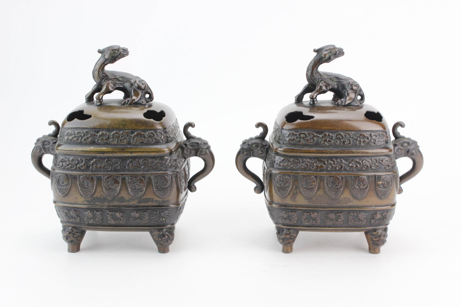 Pair of Asian Bronze Censers: Pair of Asian bronze censers of rectangular form with removable pierced covers surmounted by mythical beast finials, elephant-head handles, and raised decorative borders on four feet. Each measures