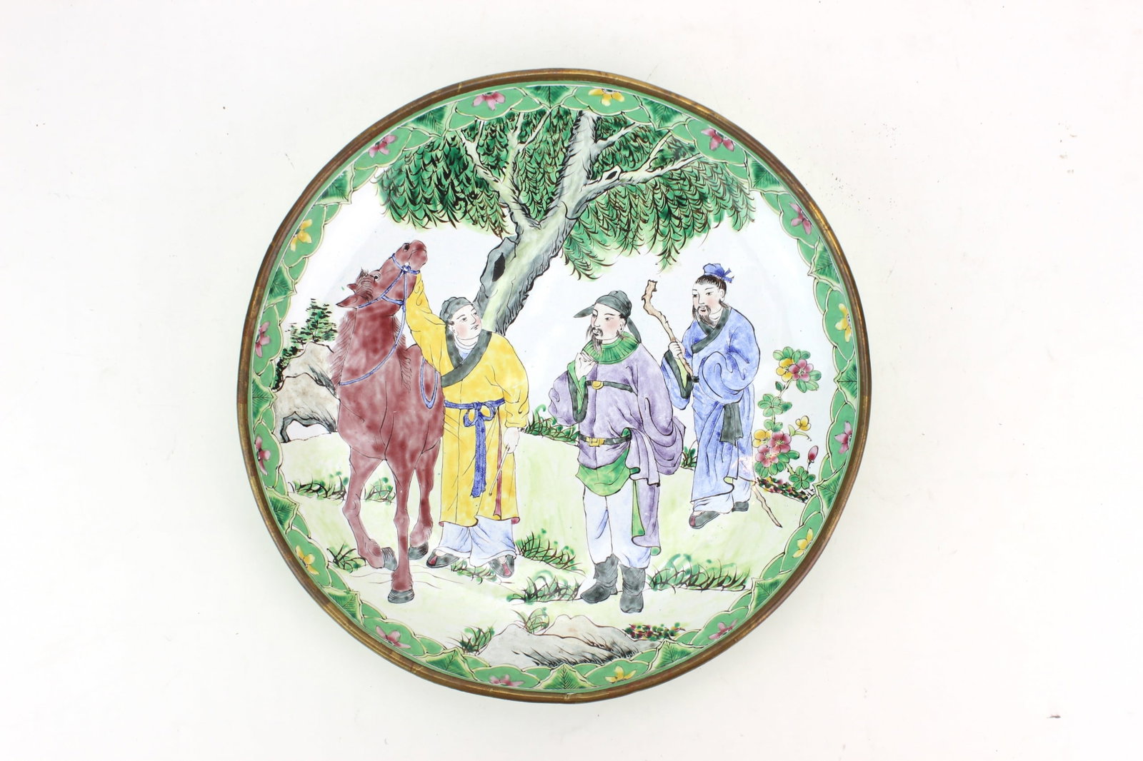 Chinese Enamel Figural Plate: Chinese enamel-decorated plate featuring a hand-painted scene of three scholars with a horse beneath a tree, framed by a green floral border. Measures approximately 7 3/4 in. (D) ? 1 1/4 in. (H).
