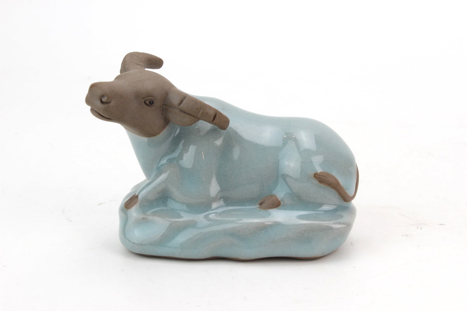 Celadon Glazed Water Buffalo Figure: Ceramic figurine depicting a reclining water buffalo with a crackle celadon-style glaze and unglazed brown head and horns. Measures approximately 2 1/2 in. (H) X 4 in. (L) X 2 1/4 in. (W). Condition: