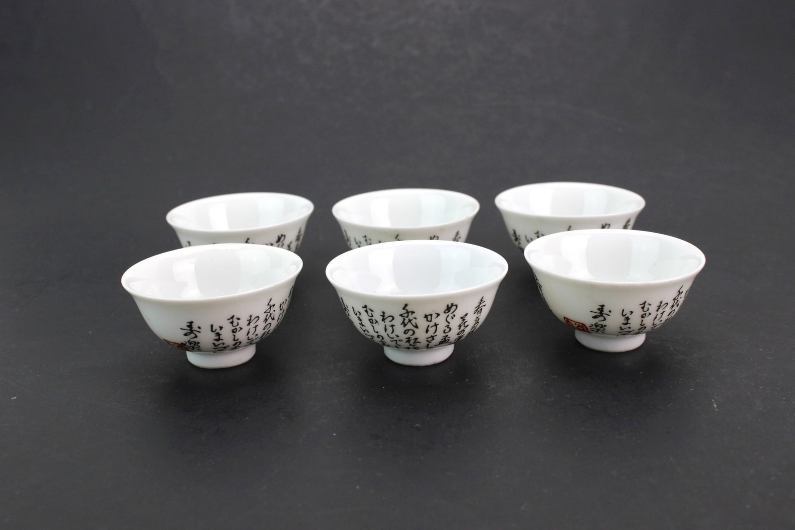 Six Japanese Porcelain Tea Bowls: A set of six Japanese porcelain tea bowls with calligraphic decoration and red seal marks, approx. 2 in. (D) X 1 in. (H), in generally good condition with minor wear and glaze imperfections.