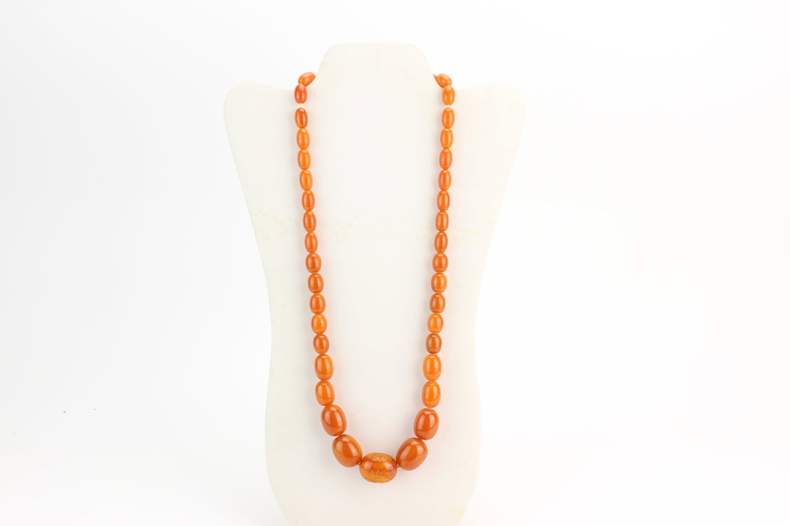 Amber Style Graduated Bead Necklace: Amber style graduated bead necklace with warm orange translucent beads and carved focal bead. Largest bead measures 1.0 inch in length; necklace measures 28 inches in length. Shows light surface