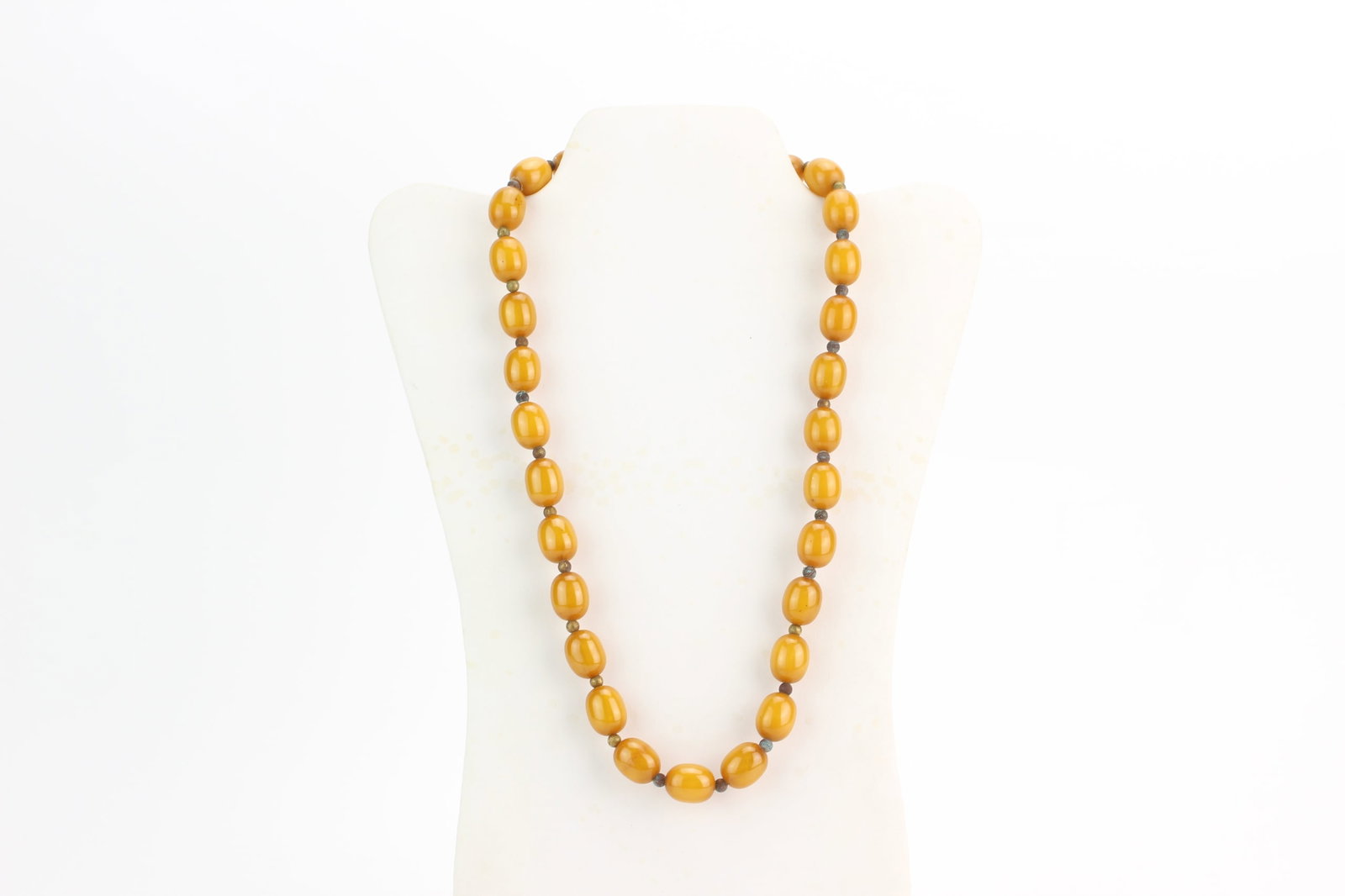 Amber Style Oval Bead Necklace: Amber style necklace composed of oval-form beads in rich butterscotch tones with metal spacer beads and clasp. Each bead measures approximately 15 mm in length; necklace measures 24 inches in length. 