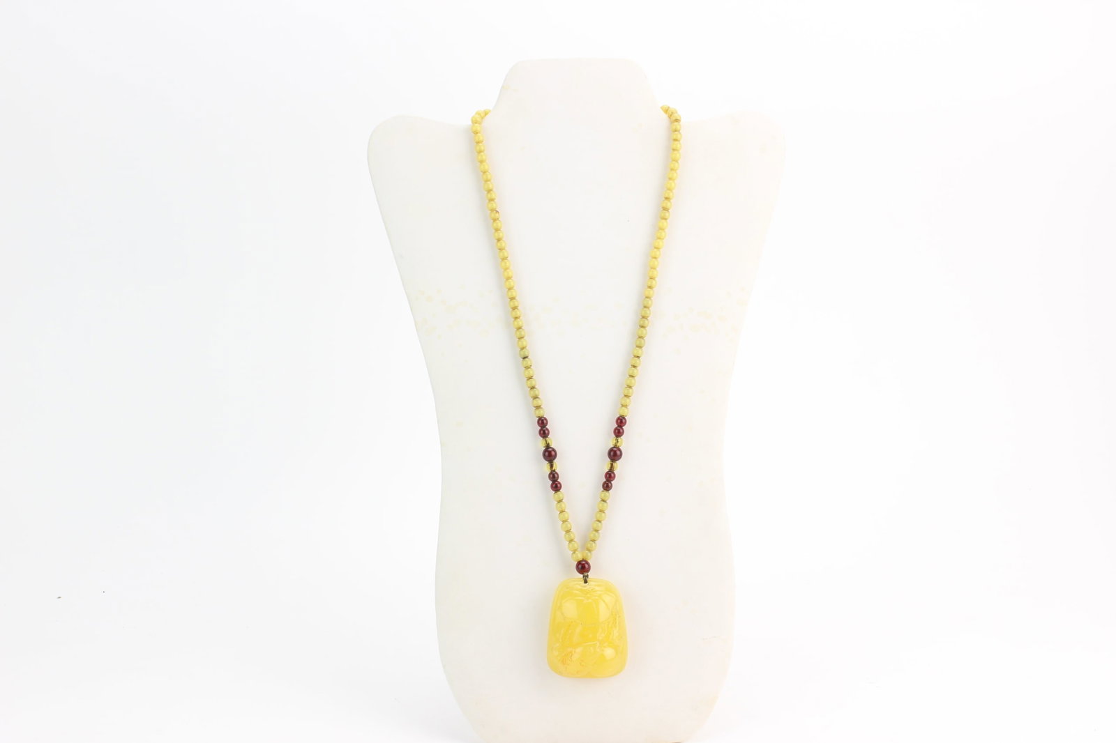 Amber Style Pendant Bead Necklace: Amber style necklace with pale yellow beads and carved pendant accented by dark red spacer beads. The pendant measures approximately 2 in. (L) x 1 1/2 in. (W) x 1.0 in. (H); necklace measures 26