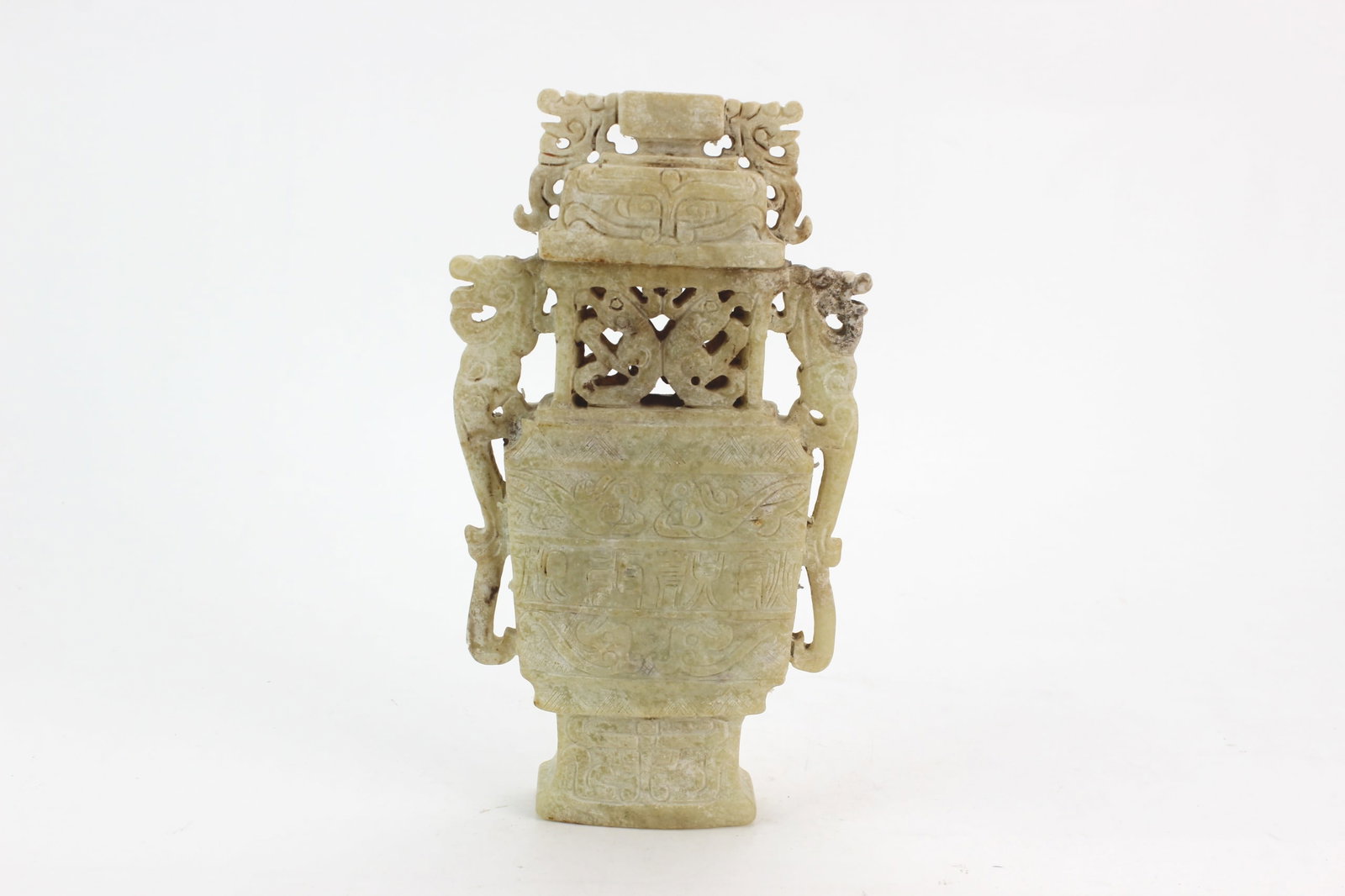 Chinese Pale Jade Archaic Vessel: Chinese pale jade archaic-style vase with openwork carving, mask motifs, and ring-form handles. Measures approximately 7 3/4 in. (H) X 4 1/2 in. (L) X 1 1/4 in. (W). Shows natural stone inclusions, su