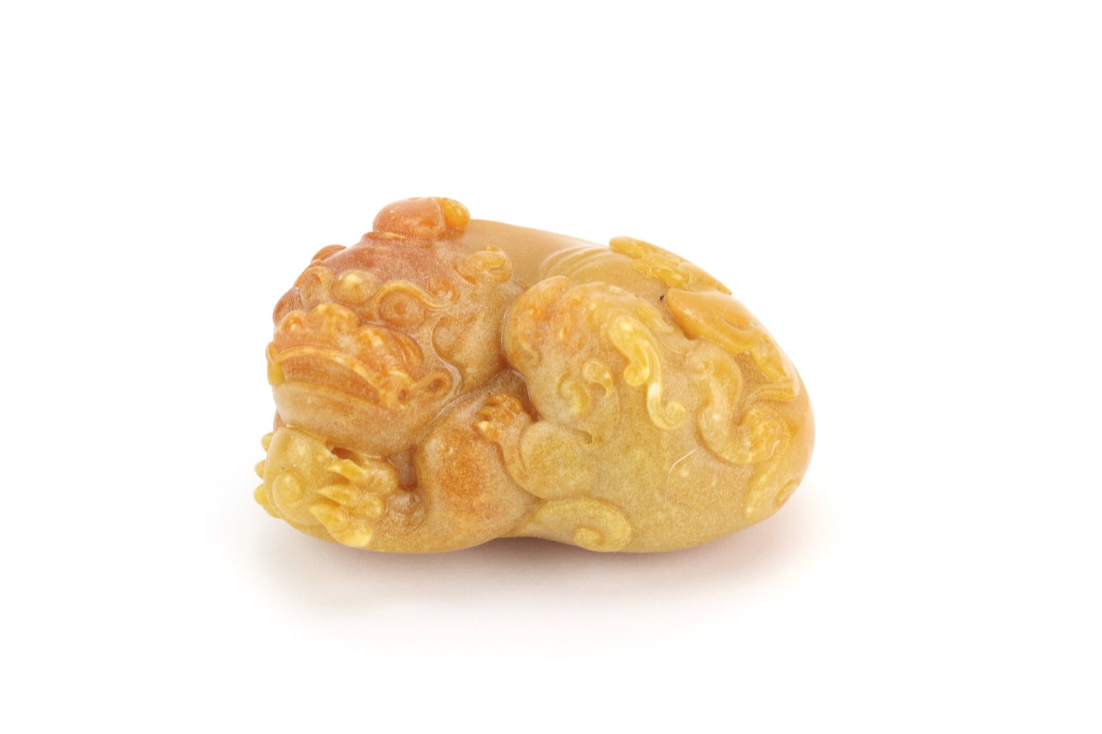 Chinese Soapstone Style Pixiu Carving: Chinese soapstone style carving depicting a recumbent pixiu mythical beast with scrolling details and amber-tone coloration. Measures approximately 3 in. (L) x 2 in. (W) x 2 in. (H). Exhibits light
