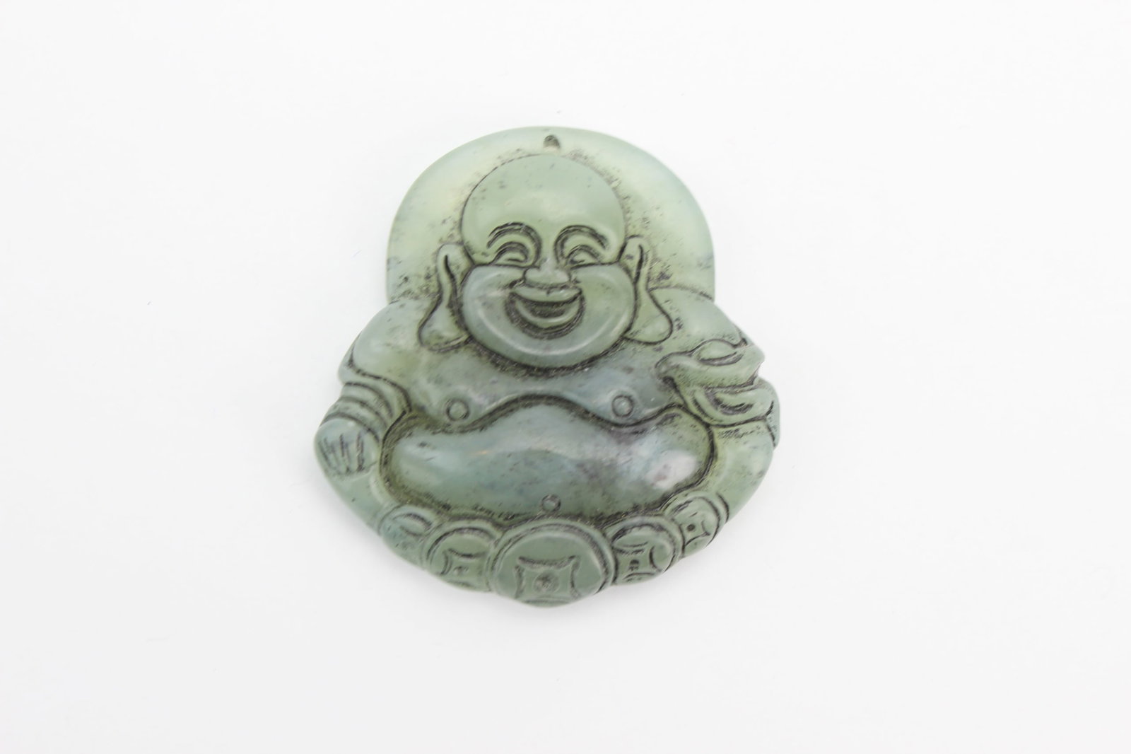 Chinese Jade Carved Laughing Buddha Pendant: Chinese pale green jade pendant carved in relief with a seated Laughing Buddha, depicted smiling and holding a sack, with coin motifs along the base and a suspension hole at the top. Measures 2 in.