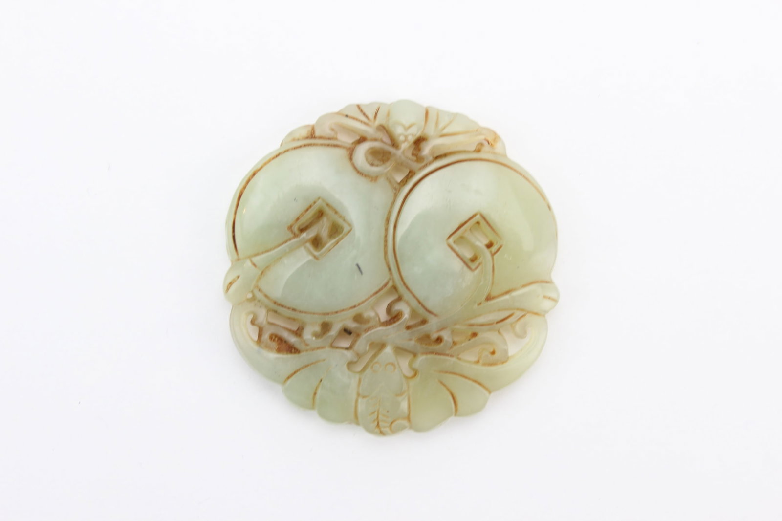 Chinese Jade Double Coin Carving: Chinese pale celadon jade carving depicting a pair of coins with scrolling leafy branches, with carved geometric details and russet-toned accents. Measures 2 1/4 in. (L) X 2 1/4 in. (W). Condition: