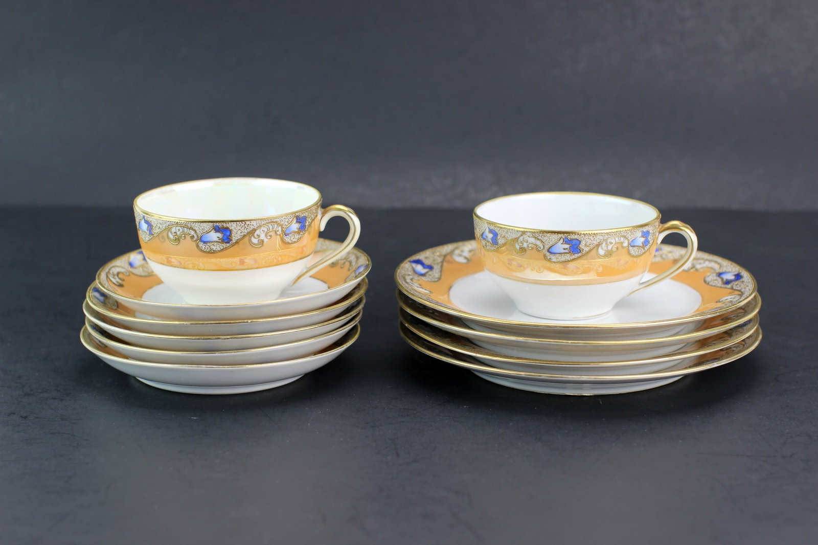 11 Pcs of Japanese Noritake Teaset: Group of 11 Japanese Noritake hand-painted porcelain items including 2 cups, 5 saucers, and 4 plates with gilt and blue decoration. Sizes: cups 3 1/2 in. (D) x 2 in. (H); saucers 5 1/2 in. (D); plates