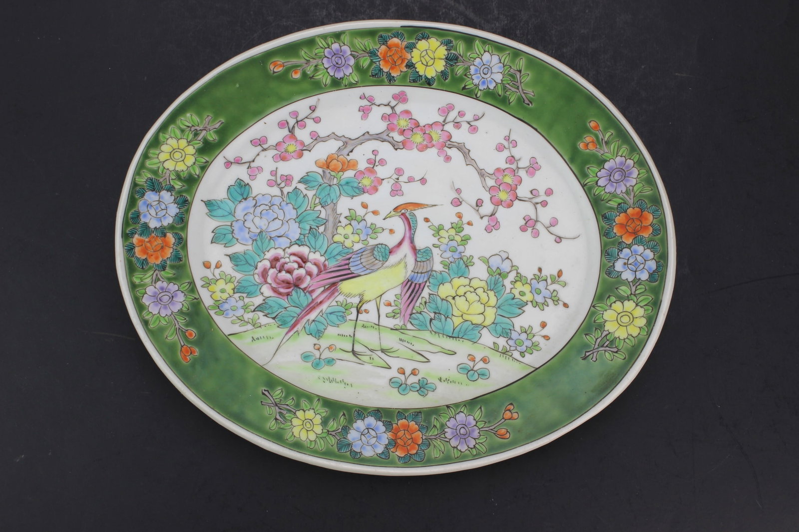 Nippon Famille Rose Style Porcelain Platter: Japanese Nippon porcelain oval platter decorated in famille rose style with a colorful bird amid peonies, flowering branches, and floral borders on a green ground. Underside bears a red ?Nippon?
