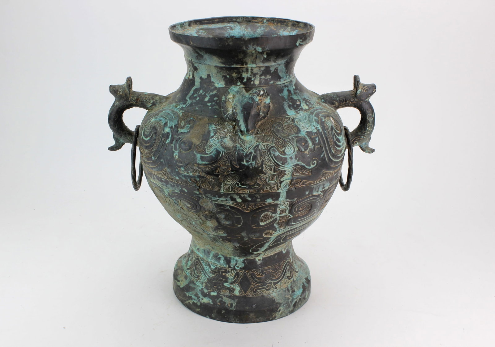 Chinese Archaistic Style Bronze Vase: A Chinese archaistic-style vases with relief geometric and stylized animal motifs, dragon-form handles with suspended rings, and extensive green patination. Condition: visible age-related surface