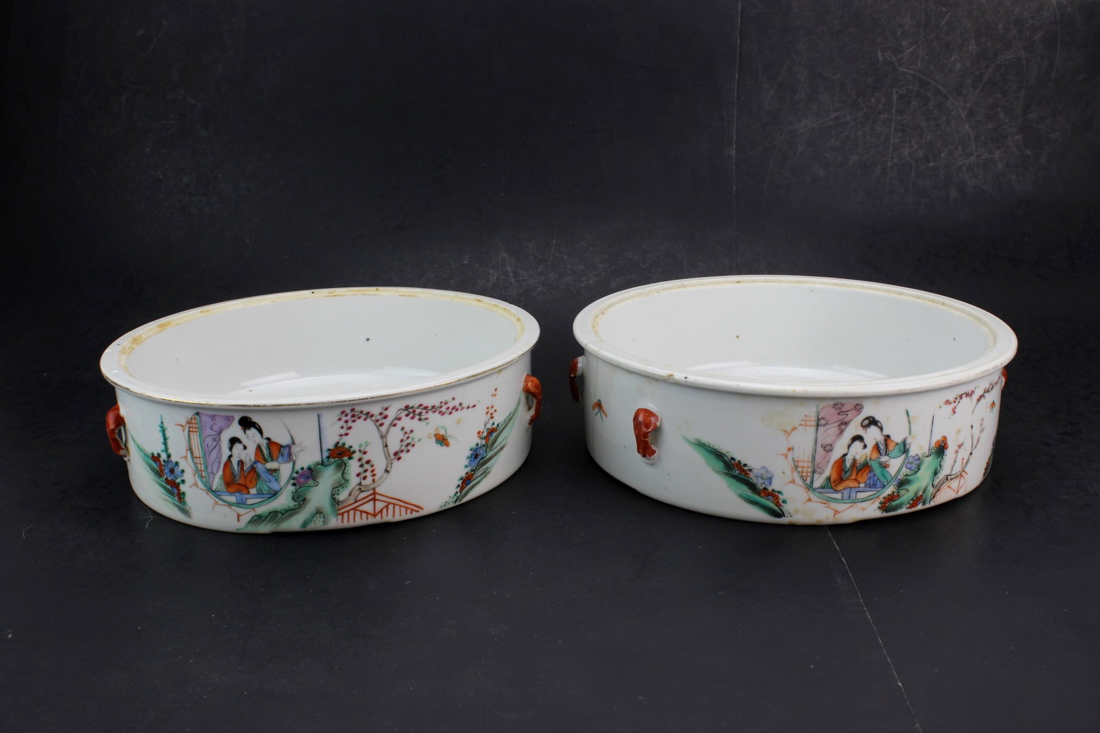 Pair Chinese Famille Rose Bowls: Pair of Chinese famille rose porcelain serving bowls with figural and landscape decoration, each having applied mask-form handles. Measure approximately 8 1/4 in. (D) x 2 1/4 in. (H). One bowl has a